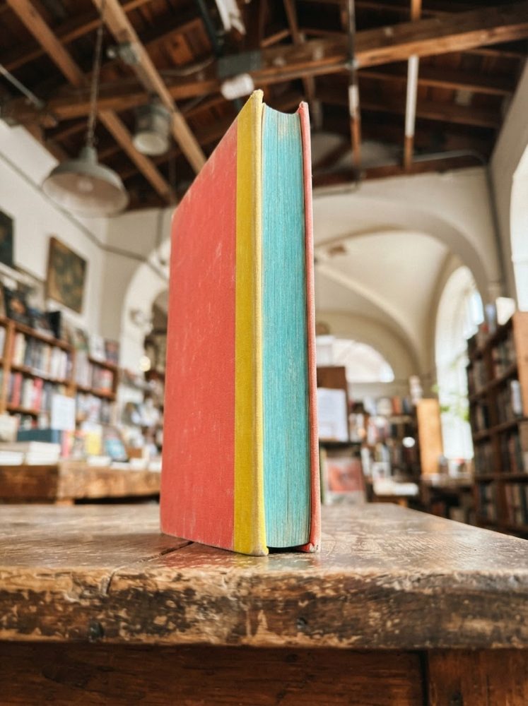 Livro colorido em pé sobre mesa de madeira numa livraria clássica com estantes e teto em madeira
