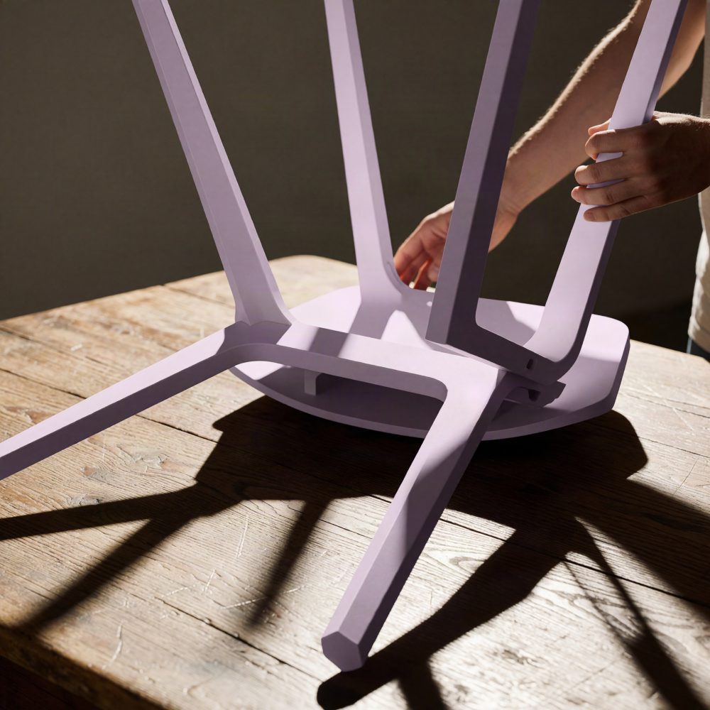 Mesa lilás invertida sobre mesa de madeira com pernas geométricas e sombras destacadas