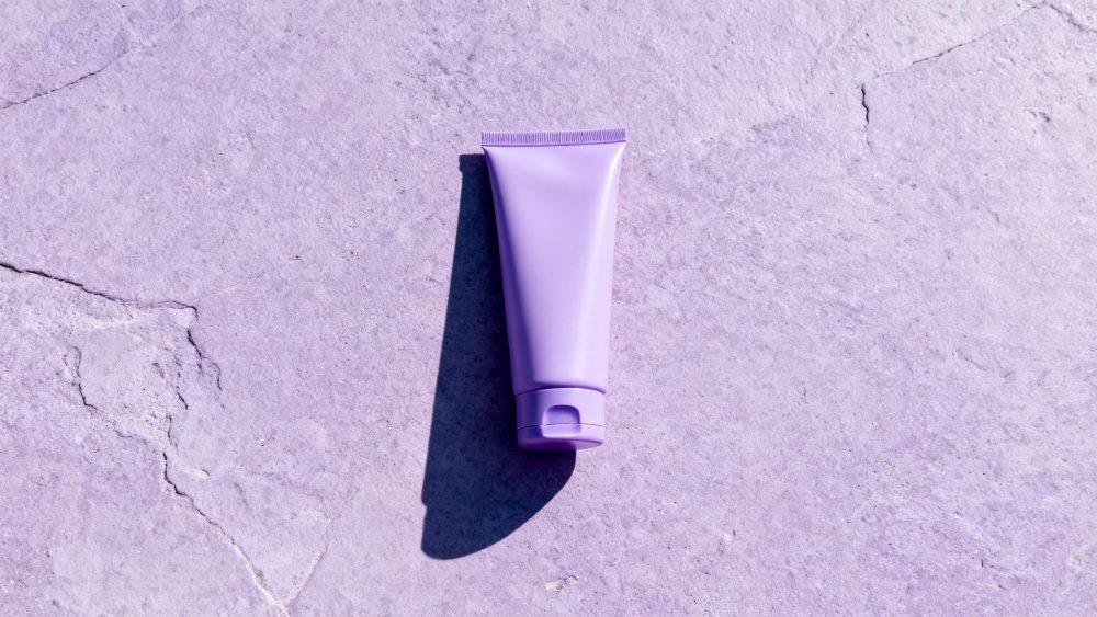 Frasco lilás de creme com tampo fechado sobre pedra lilás texturada