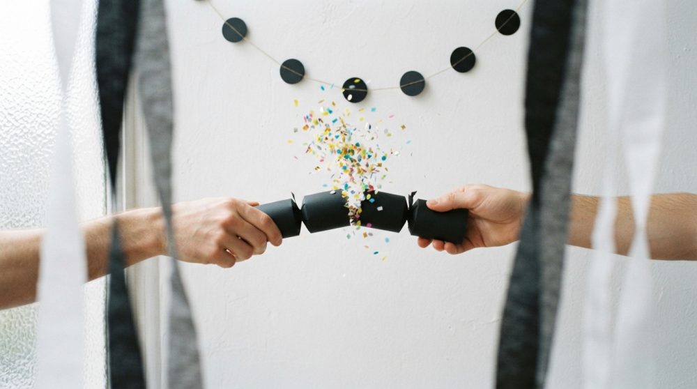 Duas mãos partem um rasgadela preto e saem confettis coloridos