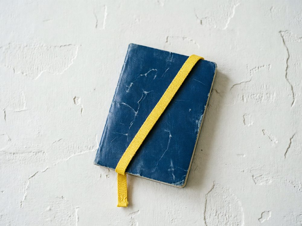 Caderno de capa azul com elástico amarelo sobre fundo branco texturizado