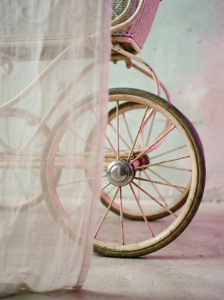 Roda antiga de carrinho de bebé vintage branca com cortina translúcida rosa ao lado