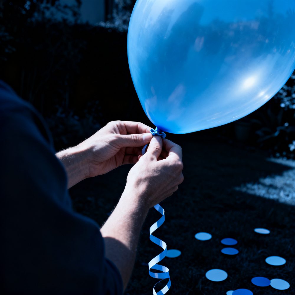 Mãos a atar fita azul numa base de balão azul num jardim escuro com decoração em azul