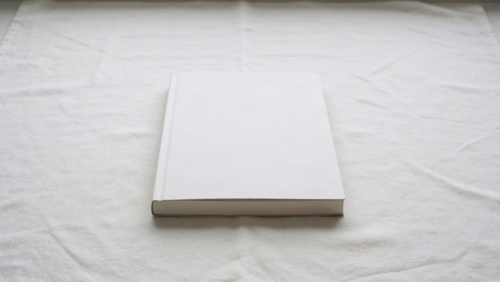 Livro fechado de capa branca sobre tecido branco levemente dobrado