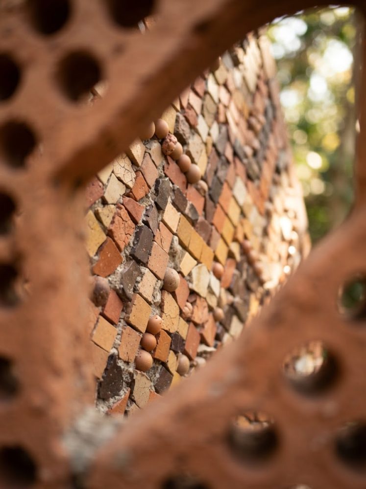 Mosaico abstrato com pequenos tijolos e esferas em tons de terra, com vista através de buracos irregulares