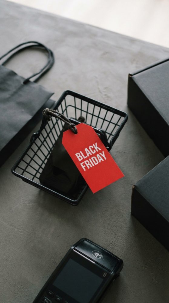 Cesta preta com etiqueta vermelha Black Friday, saco e caixas escuras e terminal de pagamento sobre superfície cinzenta
