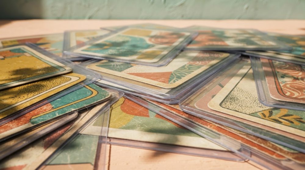 Conjunto de cartas de colecionismo protegidas por capas plásticas dispostas sobre uma superfície clara