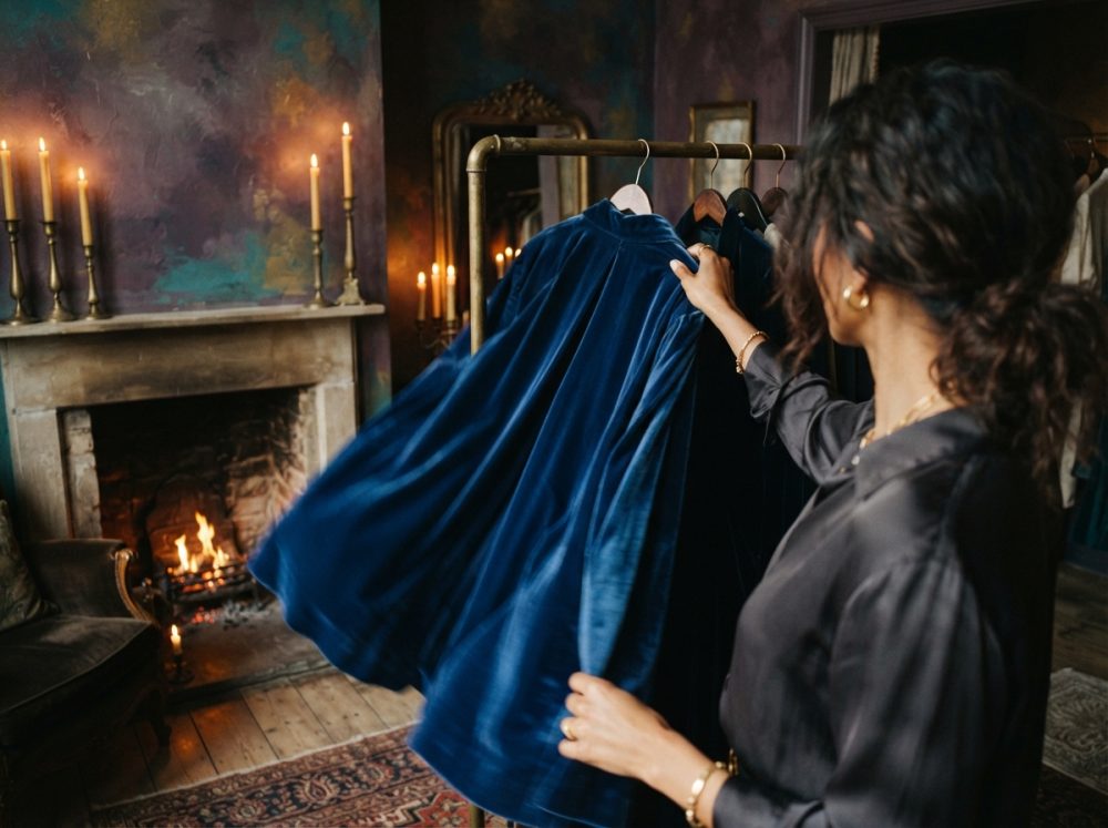 Mulher a escolher casaco azul de veludo perto de lareira com velas acesas num quarto elegante