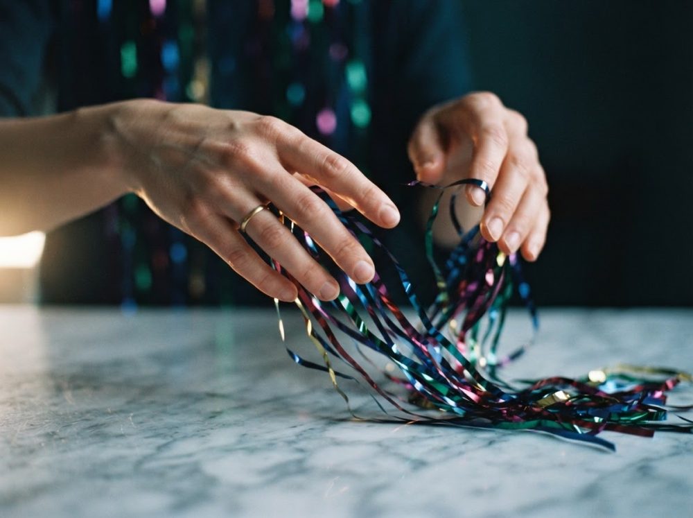 Mãos segurando fitas metálicas coloridas sobre mesa de mármore