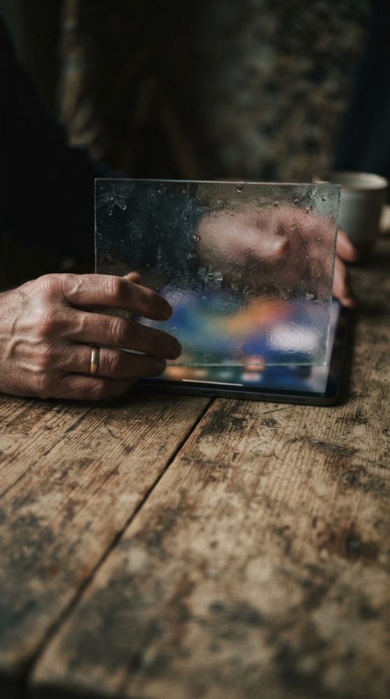 Mãos a segurar painel translúcido diante de tablet sobre mesa de madeira
