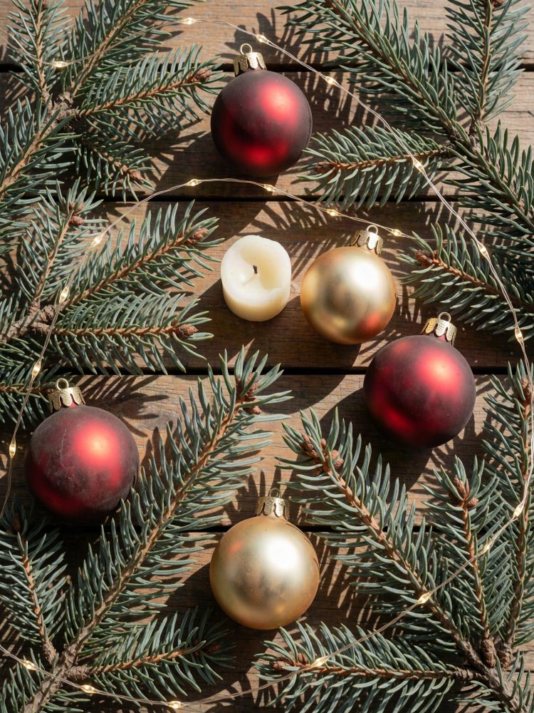 Decoração de Natal com bolas vermelhas e douradas, vela branca e ramos de pinheiro sobre madeira