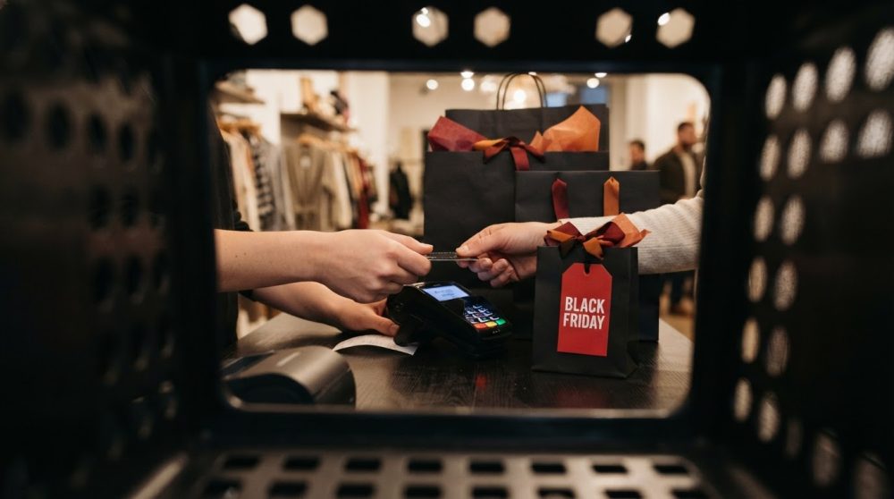 Pessoa a pagar com cartão na caixa com sacos pretos de Black Friday e roupa à venda