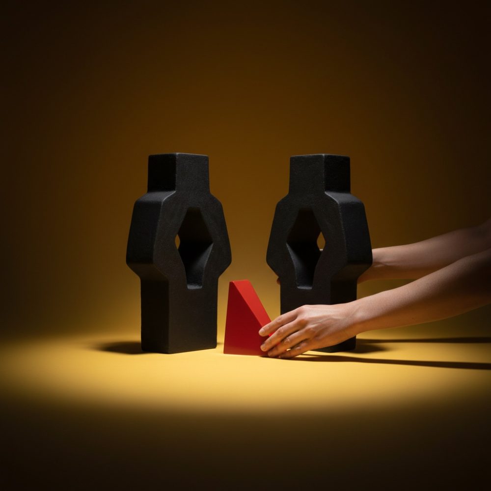 Duas esculturas abstratas negras com forma aberta seguram uma figura triangular vermelha com fundo amarelo