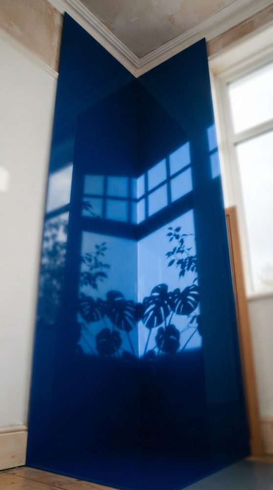 Superfície azul brilhante em canto refletindo janela e sombra de plantas tropicais