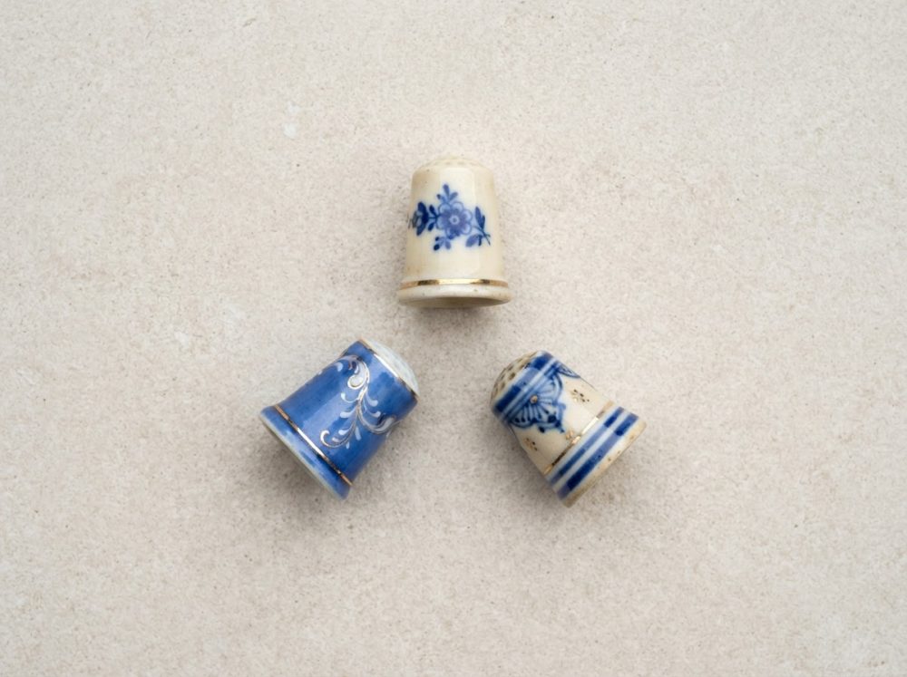 Três dedais antigos de porcelana com decoração azul e branca sobre superfície clara