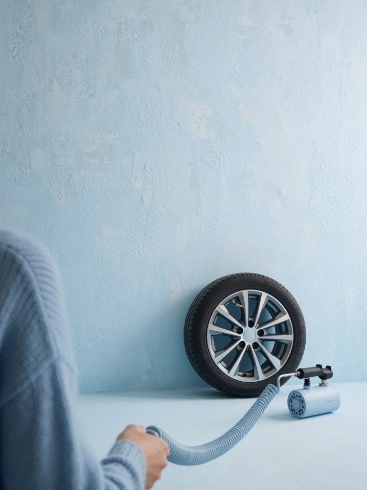 Pessoa enche pneu de automóvel com compressor de ar portátil azul e parede azul claro ao fundo