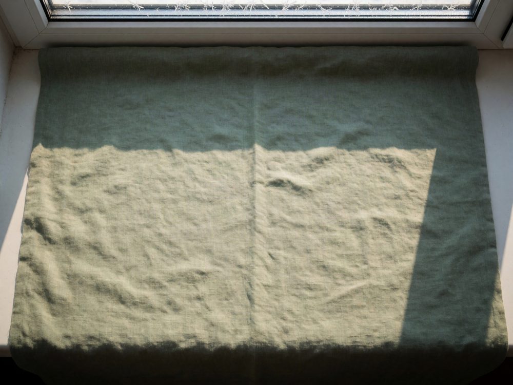 Tecido verde claro com dobras sobre peitoril branco sob luz natural com sombras