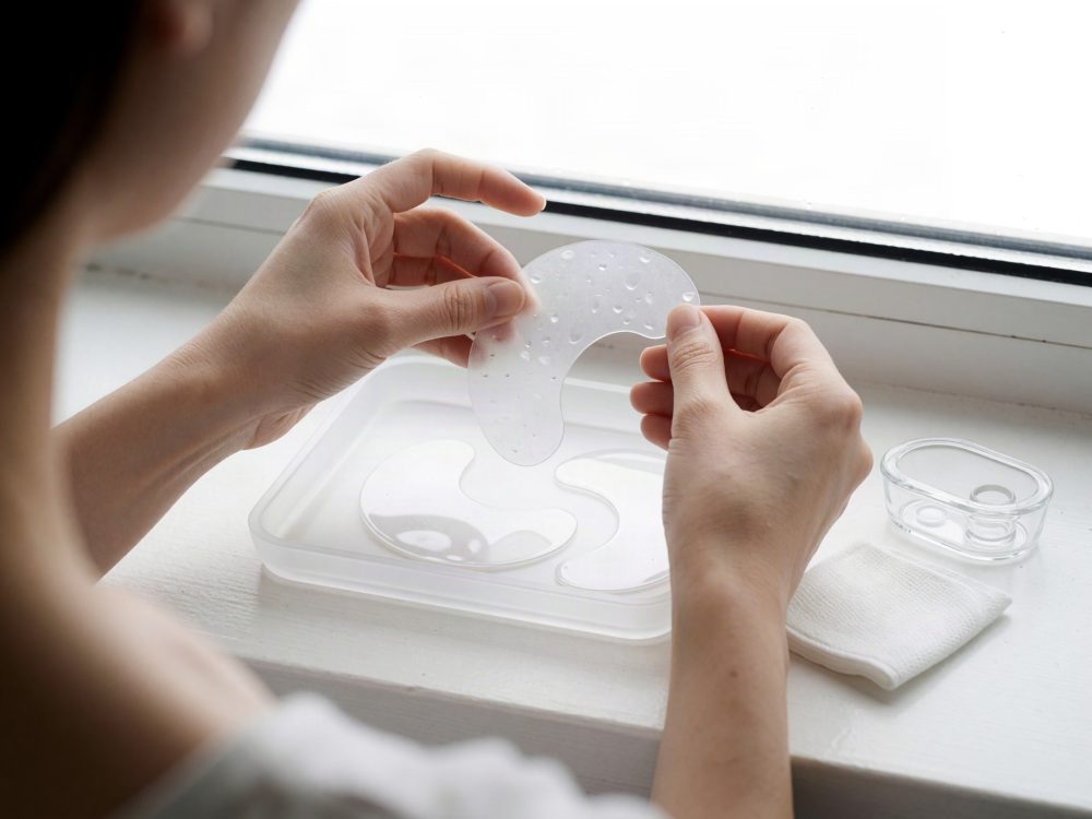 Mãos segurando máscara hidratante transparente para olhos perto de bandeja com acessórios