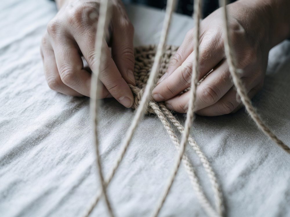 Mãos a trançar corda natural rústica sobre tecido claro para artesanato
