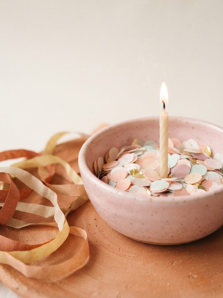 Bowl rosa com confetes coloridos e vela acesa rodeada por serpentinas coloridas