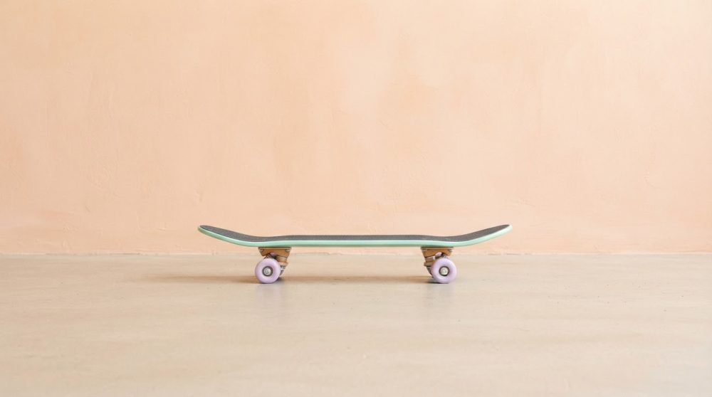 Skateboard moderno com rodas lilás sobre chão liso contra parede bege pêssego