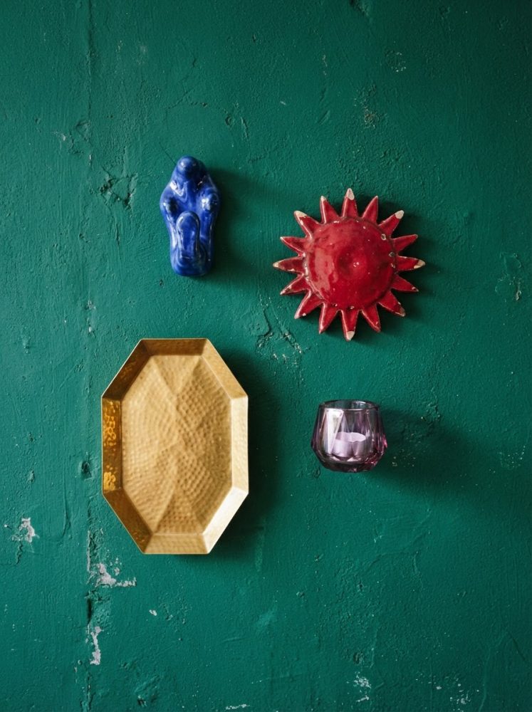 Decoração com sol vermelho, figura azul, prato dourado e castiçal roxo sobre parede verde