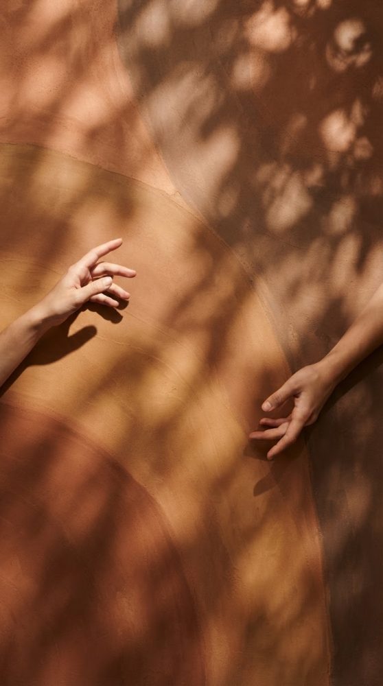 Mãos em fundo texturado com sombras naturais em tons terra e cálidos