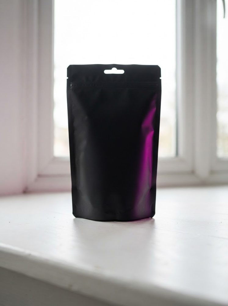 Saco preto mate com fecho zip e gancho sobre superfície branca iluminado por luz natural