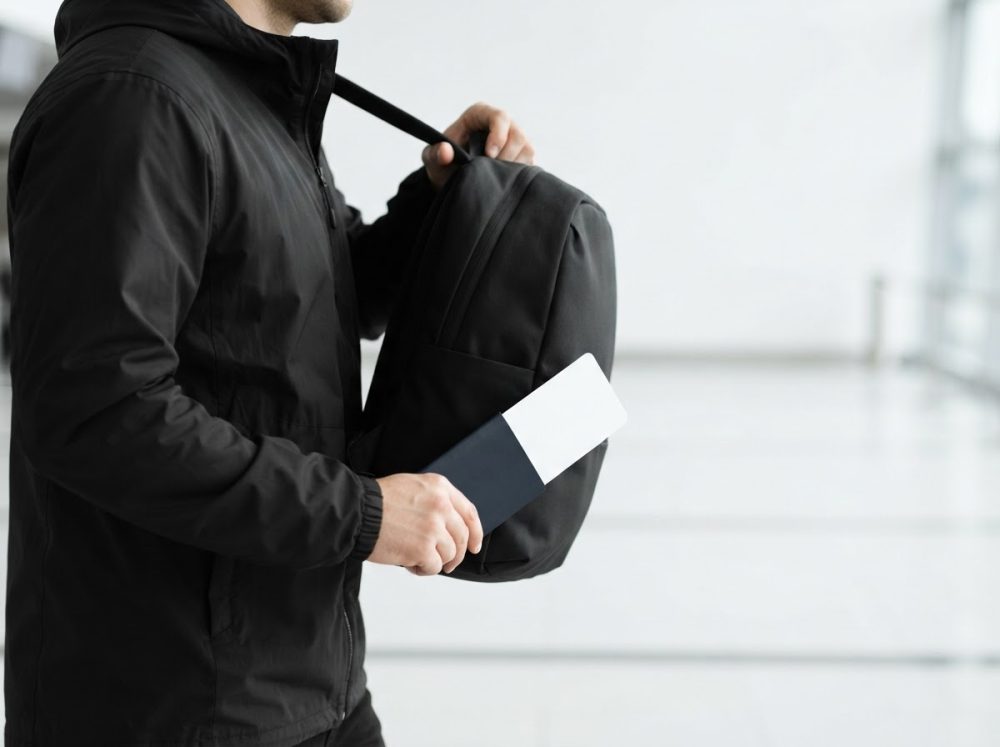Homem com mochila preta e bilhete de avião num ambiente de viagem