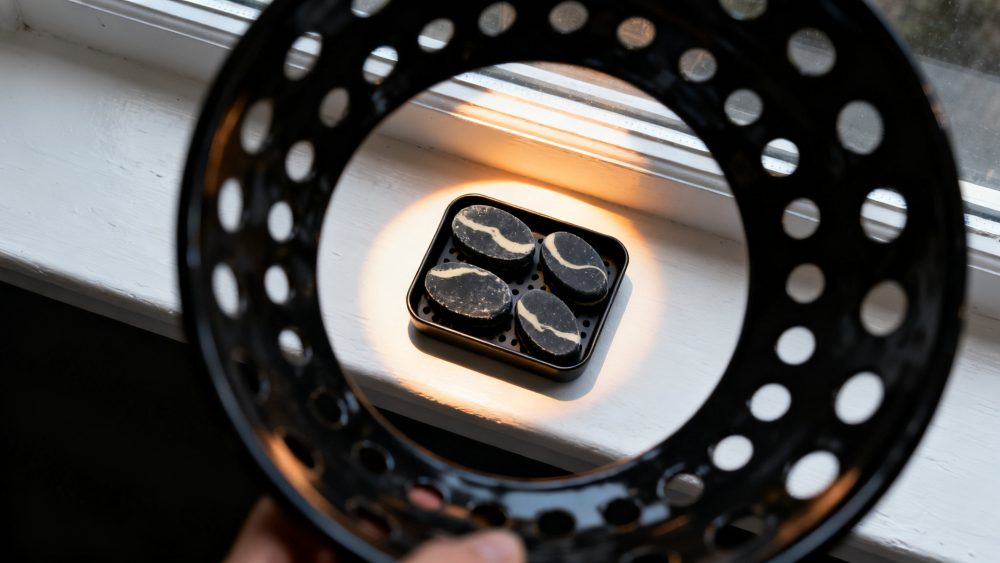 Quatro sabonetes pretos com riscas claras num suporte preto perfurado sobre uma janela branca iluminada
