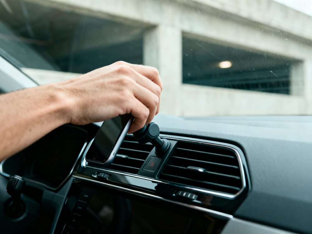 Mão a colocar telemóvel num suporte magnético fixado na ventoinha do carro