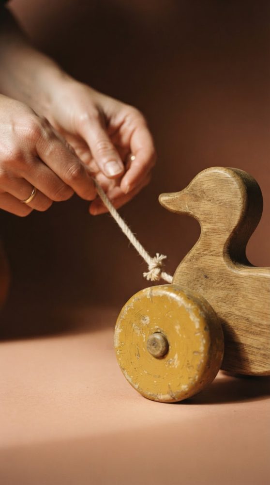 Brinquedo em madeira em forma de pato com rodas amarelas e corda a ser puxada por mãos