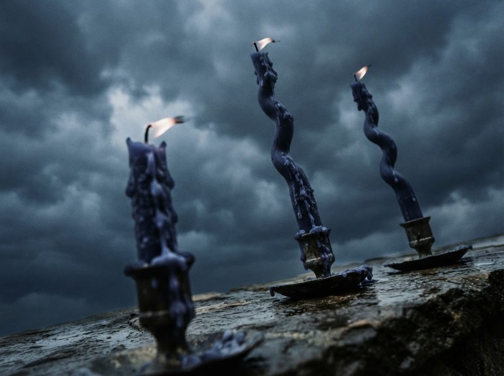 Três velas azuis retorcidas acesas sobre suportes metálicos contra céu nublado e escuro