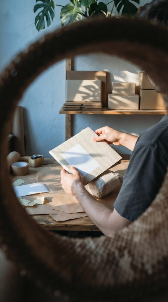 Pessoa a embalar encomenda com papel kraft e etiqueta branca em mesa com caixas e fitas