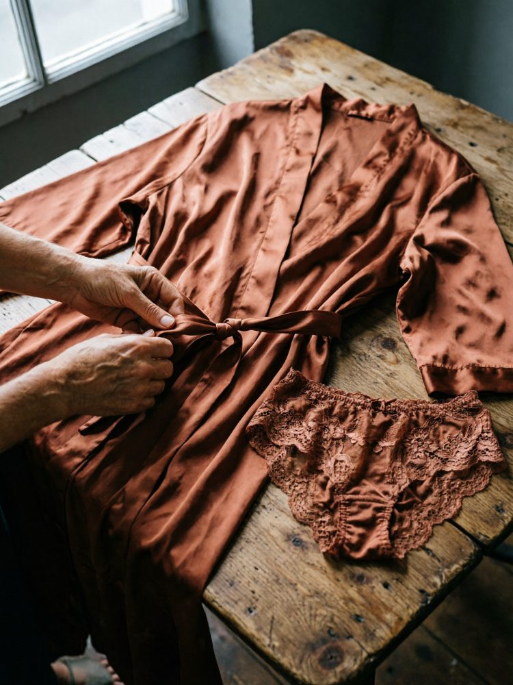 Robe de cetim castanho com cinto e cueca de renda castanha sobre mesa de madeira