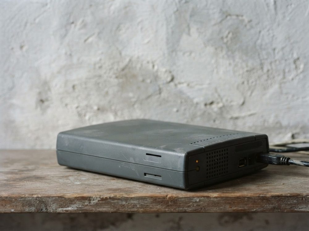 Disco rígido externo retro cinzento ligado por cabo USB em mesa de madeira rústica