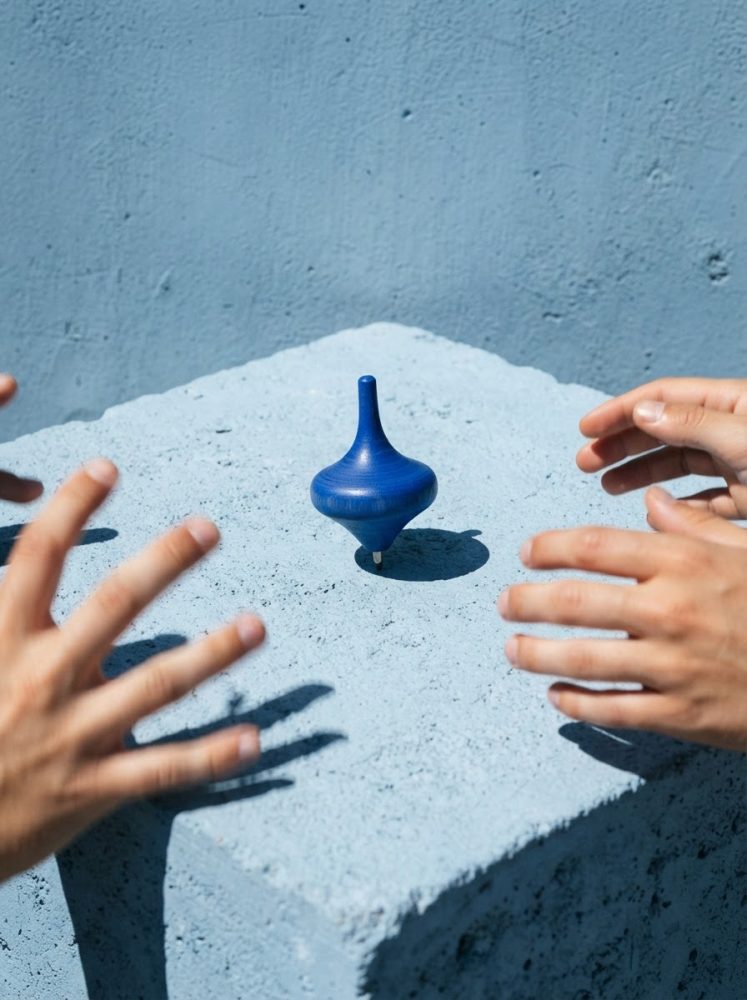 Peão de madeira azul a girar numa base azul com mãos à volta