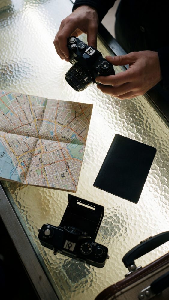 Mãos segurando câmara vintage sobre mesa com mapa, passaporte e outra câmara
