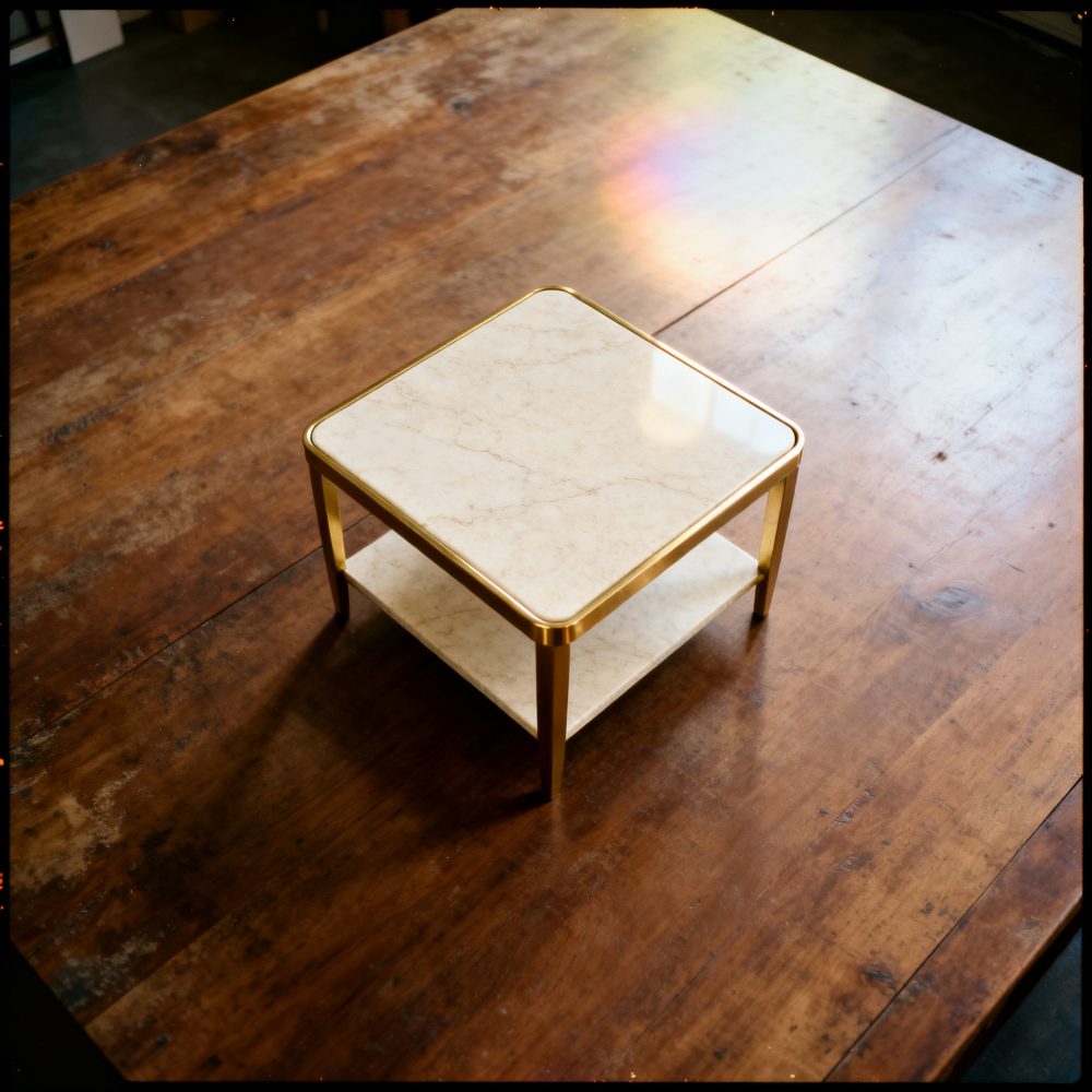 Mesa de centro quadrada com tampo de mármore e estrutura dourada sobre mesa de madeira rústica