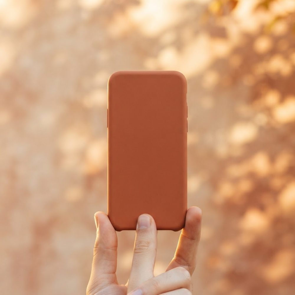 Mão segura capa de telemóvel castanha com fundo desfocado em tons quentes