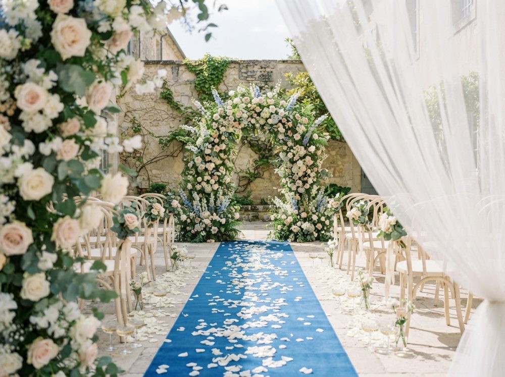 Cerimónia de casamento ao ar livre com arco floral, tapete azul e cadeiras decoradas com flores