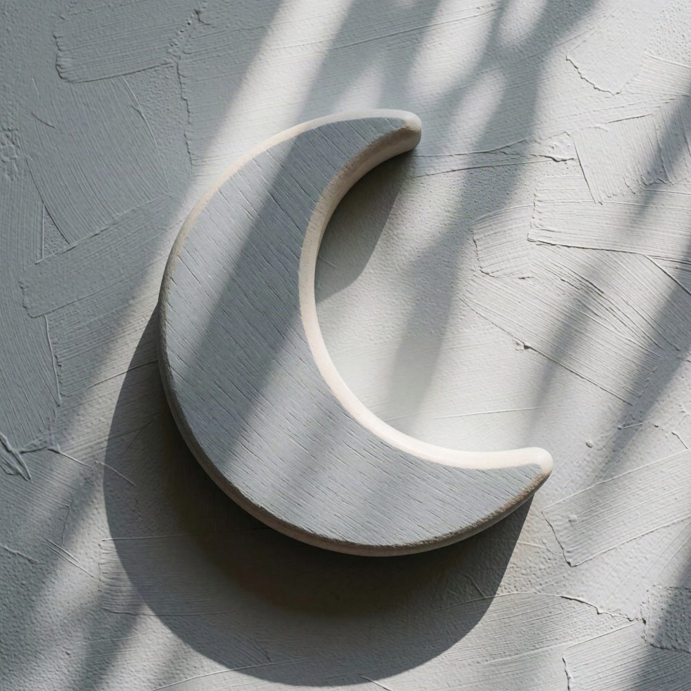 Brinquedo de madeira em forma de lua crescente sobre superfície texturada clara com sombras suaves