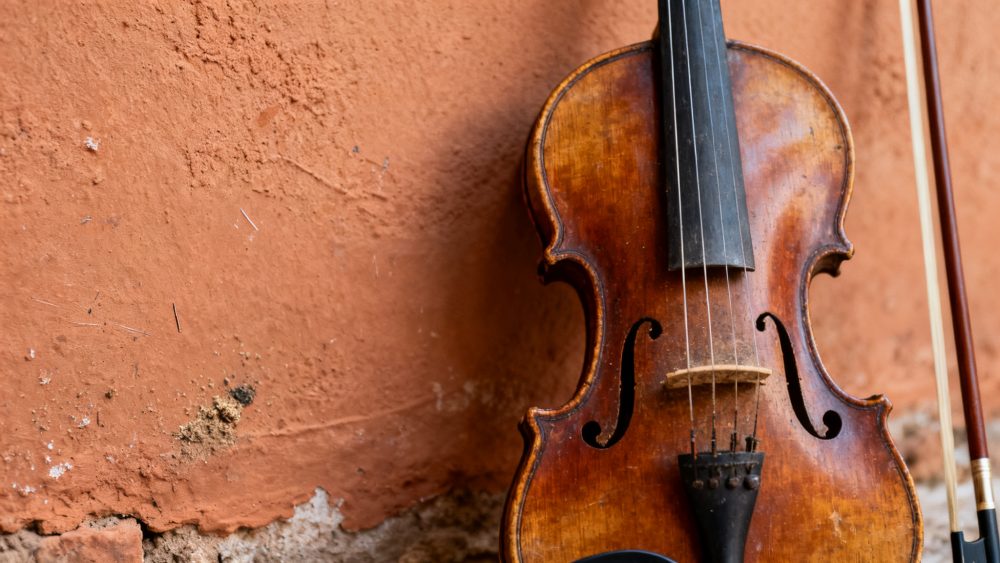 Violino envelhecido encostado em parede rústica com arco musical ao lado