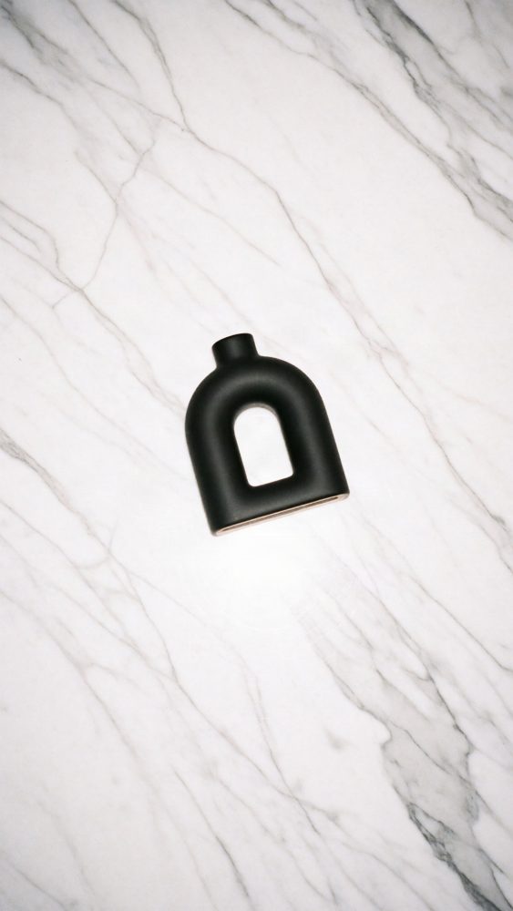 Vaso preto minimalista sobre superfície de mármore branco com veios cinzentos