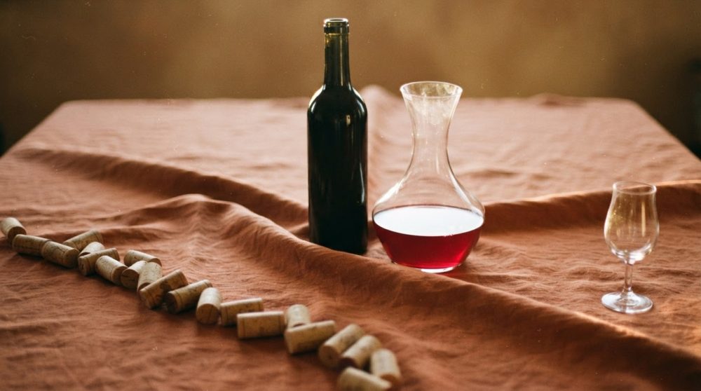 Garrafa de vinho, decantador com vinho tinto, cálice e vários rolhas sobre tecido castanho