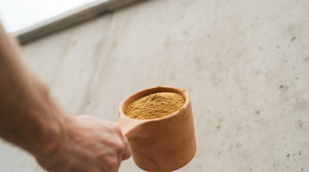 Colher de barro com suplemento em pó amarelo contra fundo neutro