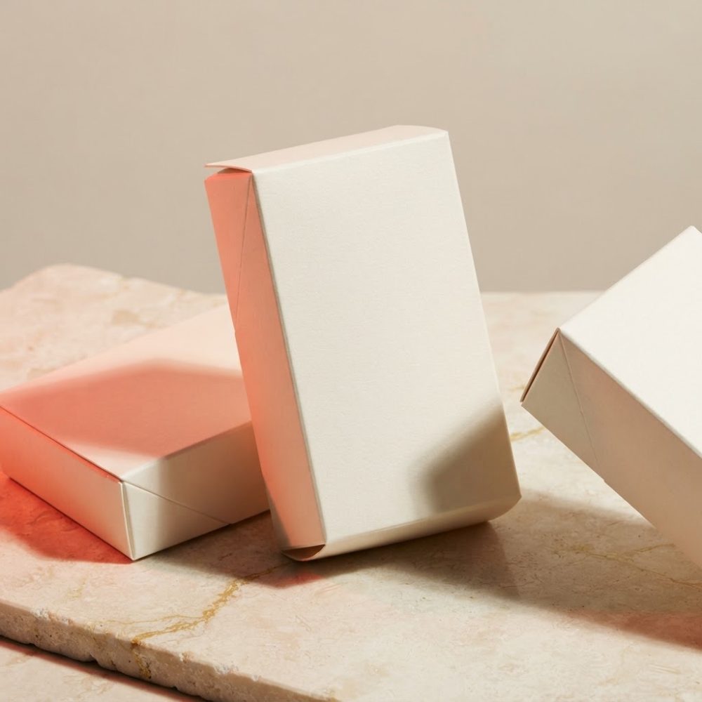 Três caixas brancas de cartão para mockup sobre pedra clara com sombra suave