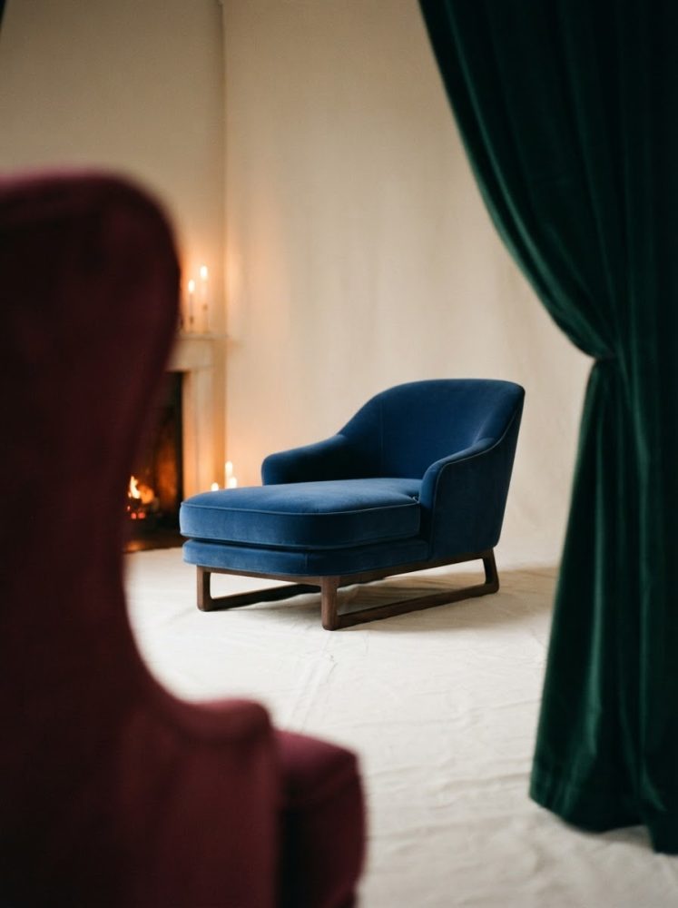 Poltrona azul de veludo perto de lareira e cortinas verdes