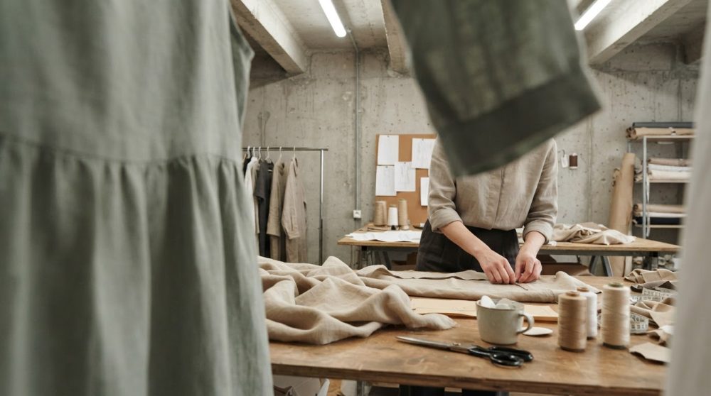Designer a trabalhar em tecidos de linho num ateliê de moda com decoração neutra e ferramentas de costura