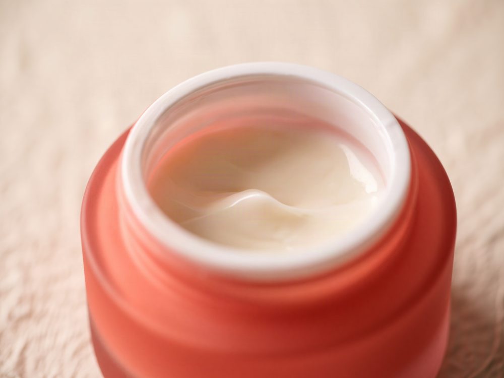Frasco rosa coral aberto com creme hidratante facial de textura cremosa branca